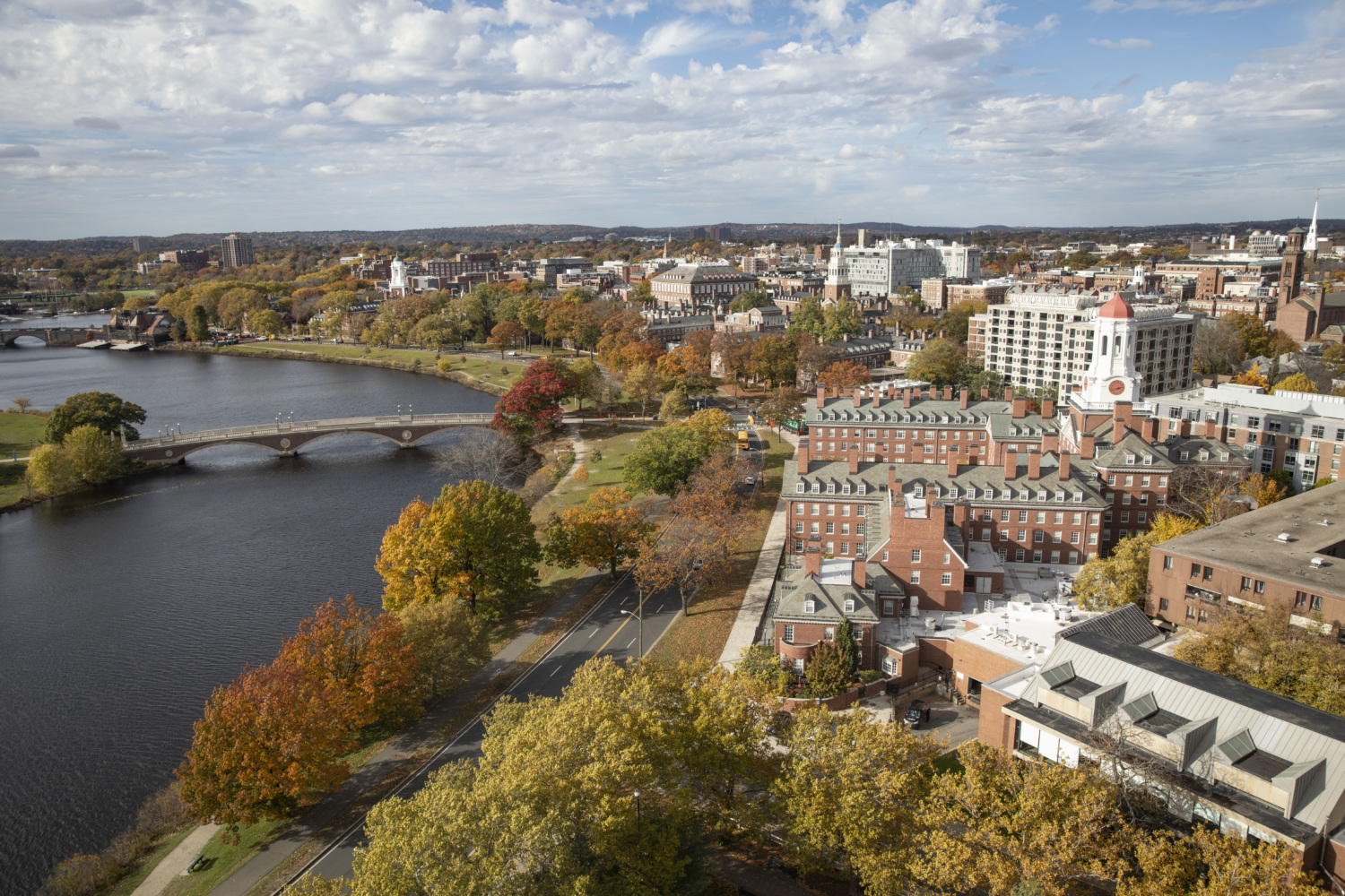 Aerial view of Harvard University with the river, trees that show colorful autumn leaves, and history brick buildings on campus.