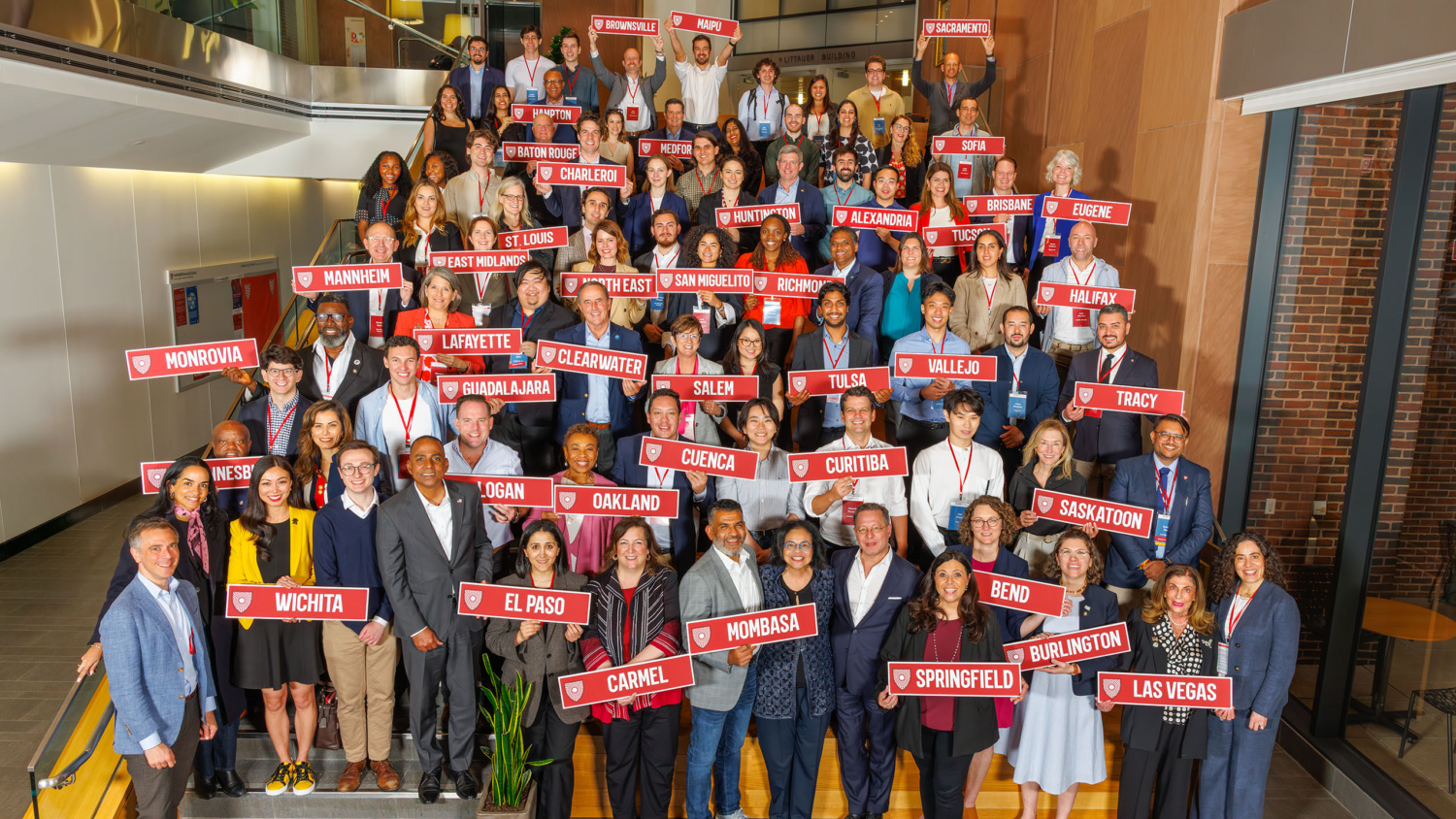 students and mayors holding signs with city names inside Harvard Kennedy School